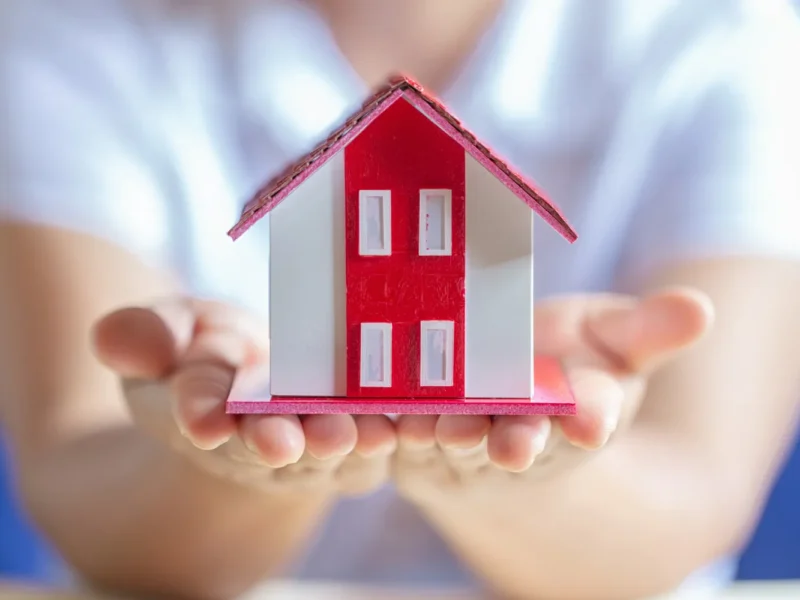 Modelo de casa en miniatura en manos de una persona, simbolizando la compra de vivienda y la propiedad inmobiliaria.