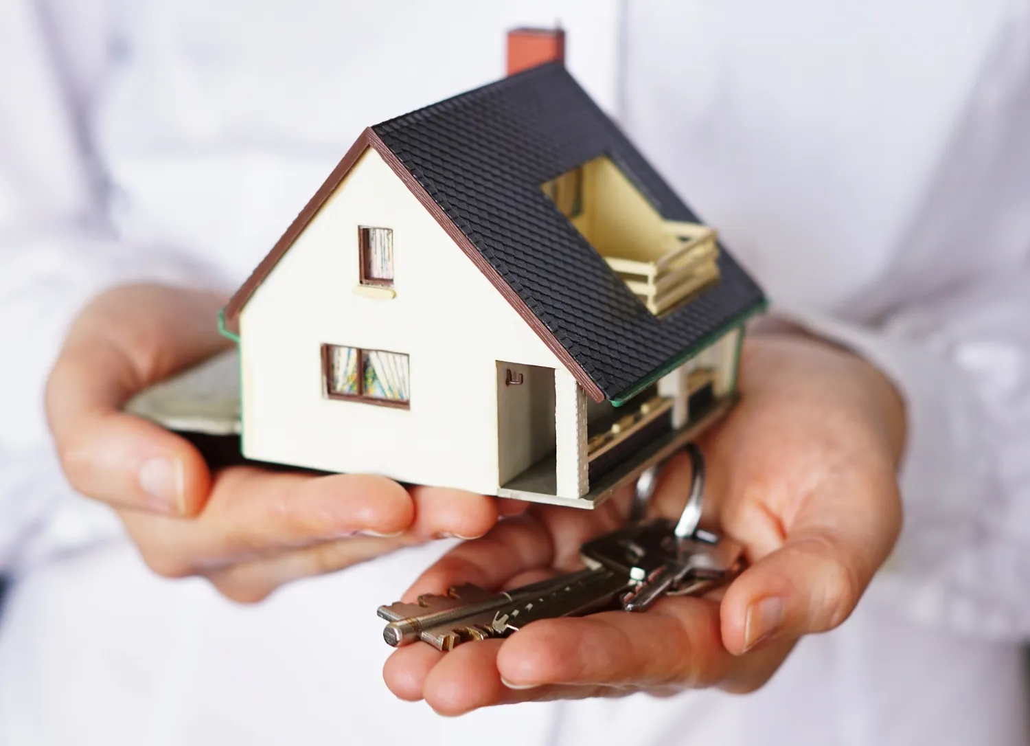 Manos sosteniendo una casa en miniatura junto a un llavero, simbolizando la compra de una vivienda y la propiedad inmobiliaria.